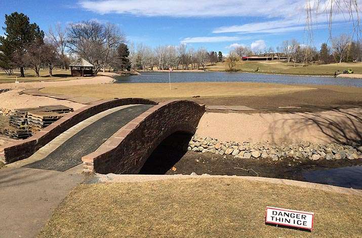17 surround is stripped and the lake slope is rebuilt with pea gravel at Cherry Hills Country Club, Cherry Hills Village, CO. The bridge is too narrow and fragile to carry big rolls of sod on to the island green.