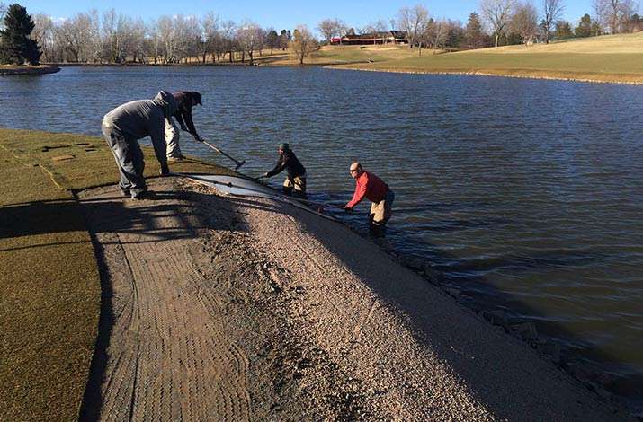 Big rolls of GVT Short Cut Bluegrass are pulled into place over the pea gravel lake bank on 17 island green at Cherry Hills Country Club March 2014 in preparation for the BMW Championship.